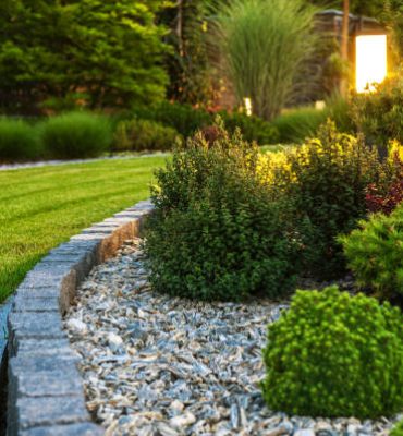 Closeup of Professionally Landscaped Flower Bed with Decorative Green Garden Plants and Evenly Mowed Lawn in the Background.